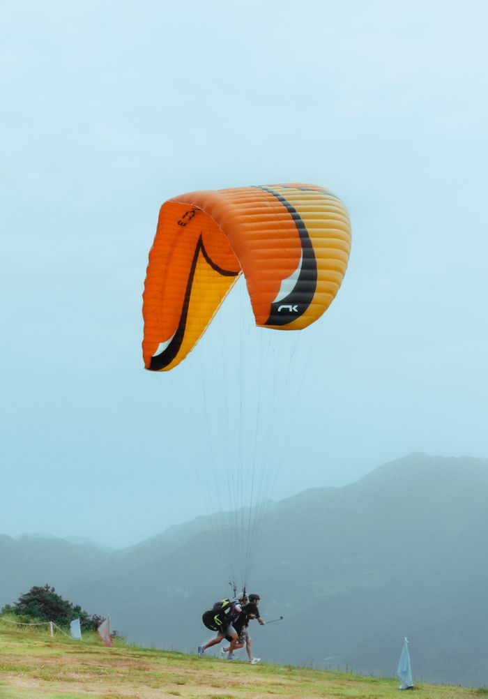 Two people paragliding above a scenic mountainous landscape on a misty day.