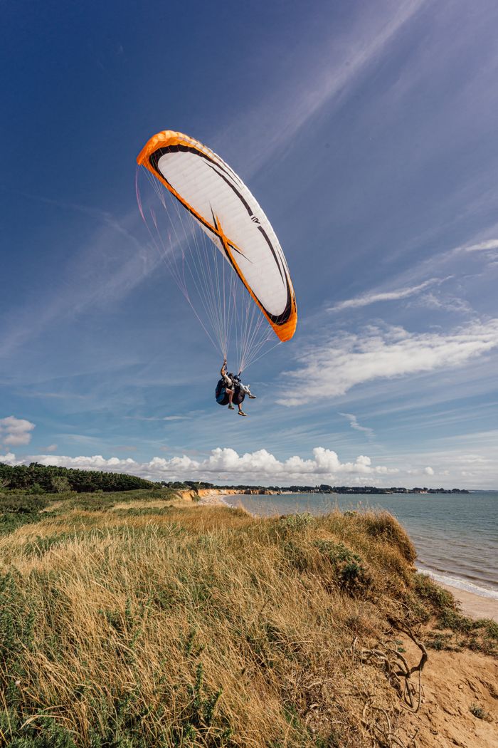 Couple paragliding over scenic cliffs of Pénestin, France on a bright summer day.