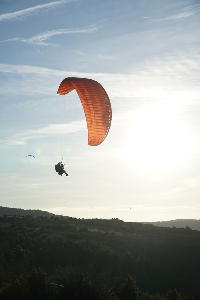 A paraglider with red wing gliding over Millau, France during a serene sunrise.