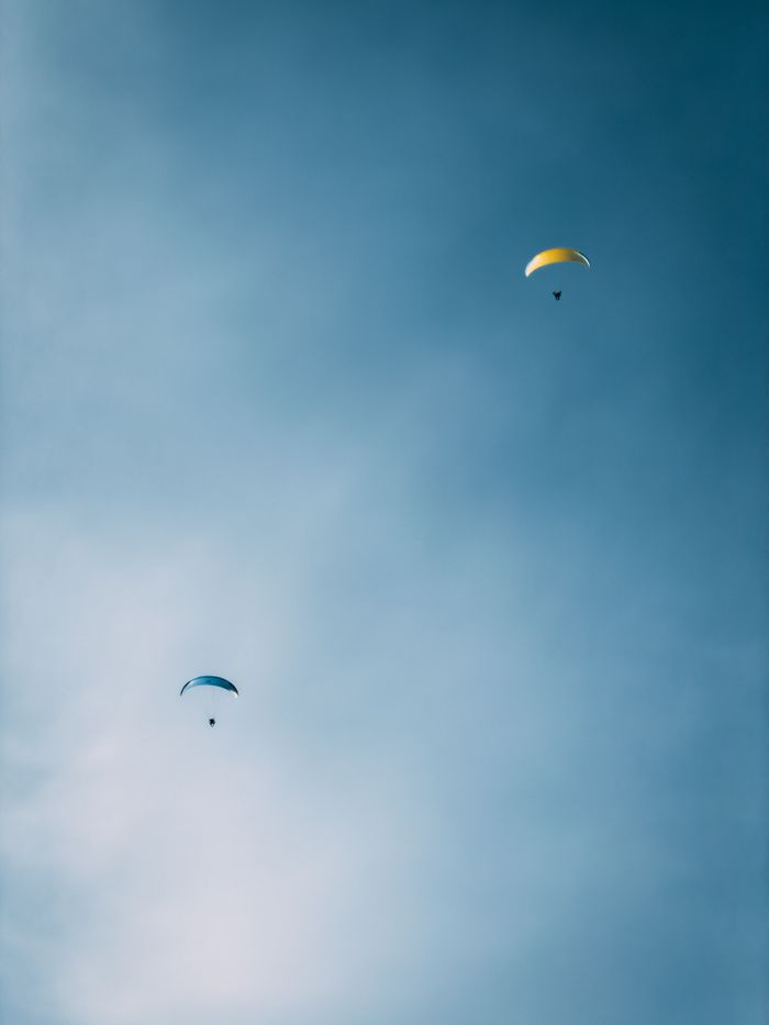 Two paragliders soar against a serene blue sky, capturing the essence of freedom.